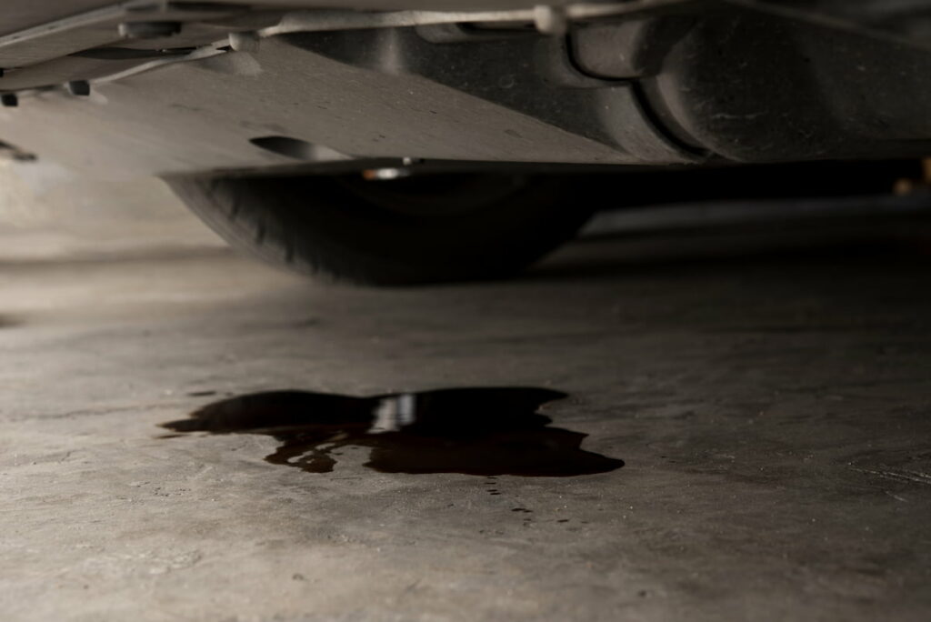 Water leaking from underneath a car onto a concrete garage floor, indicating a potential vehicle issue.